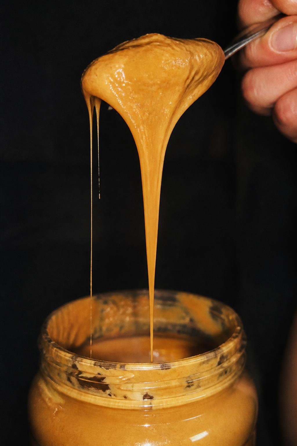 Spoon dripping golden nut butter in flash light